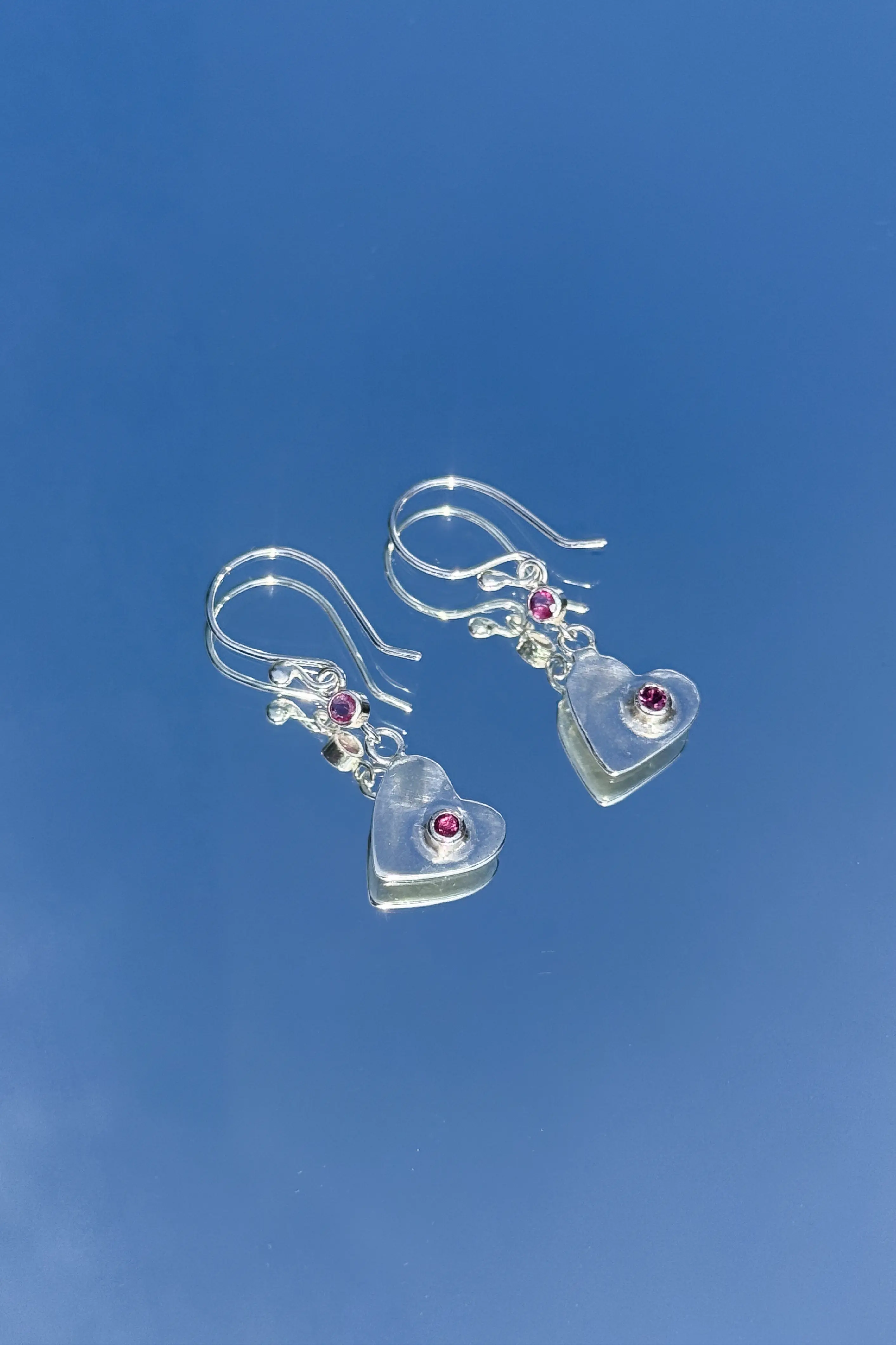 Some silver earrings with a pink gem over a bluesky background.