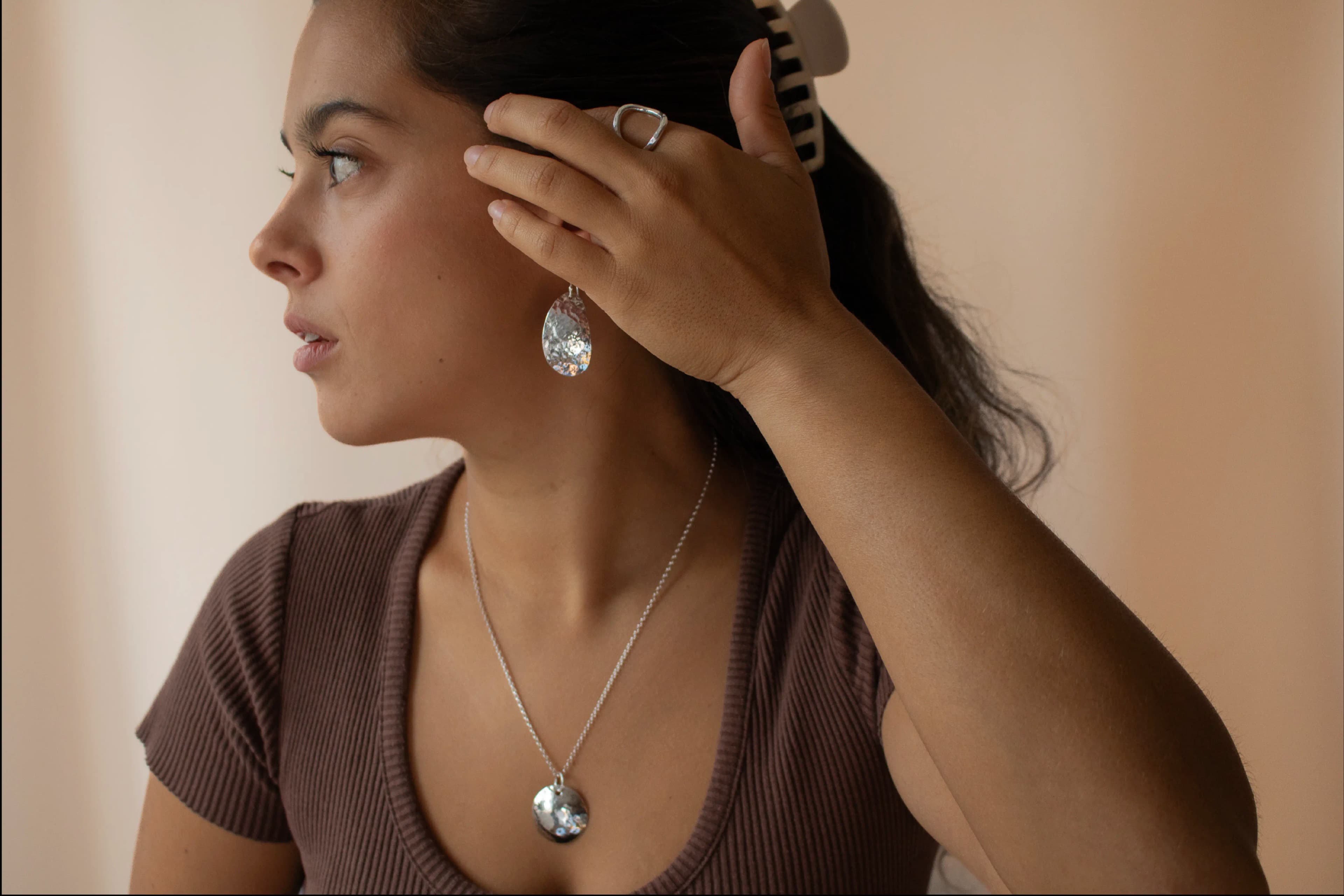 The model wearing a necklace and some discotheue earrings over a light brown background.