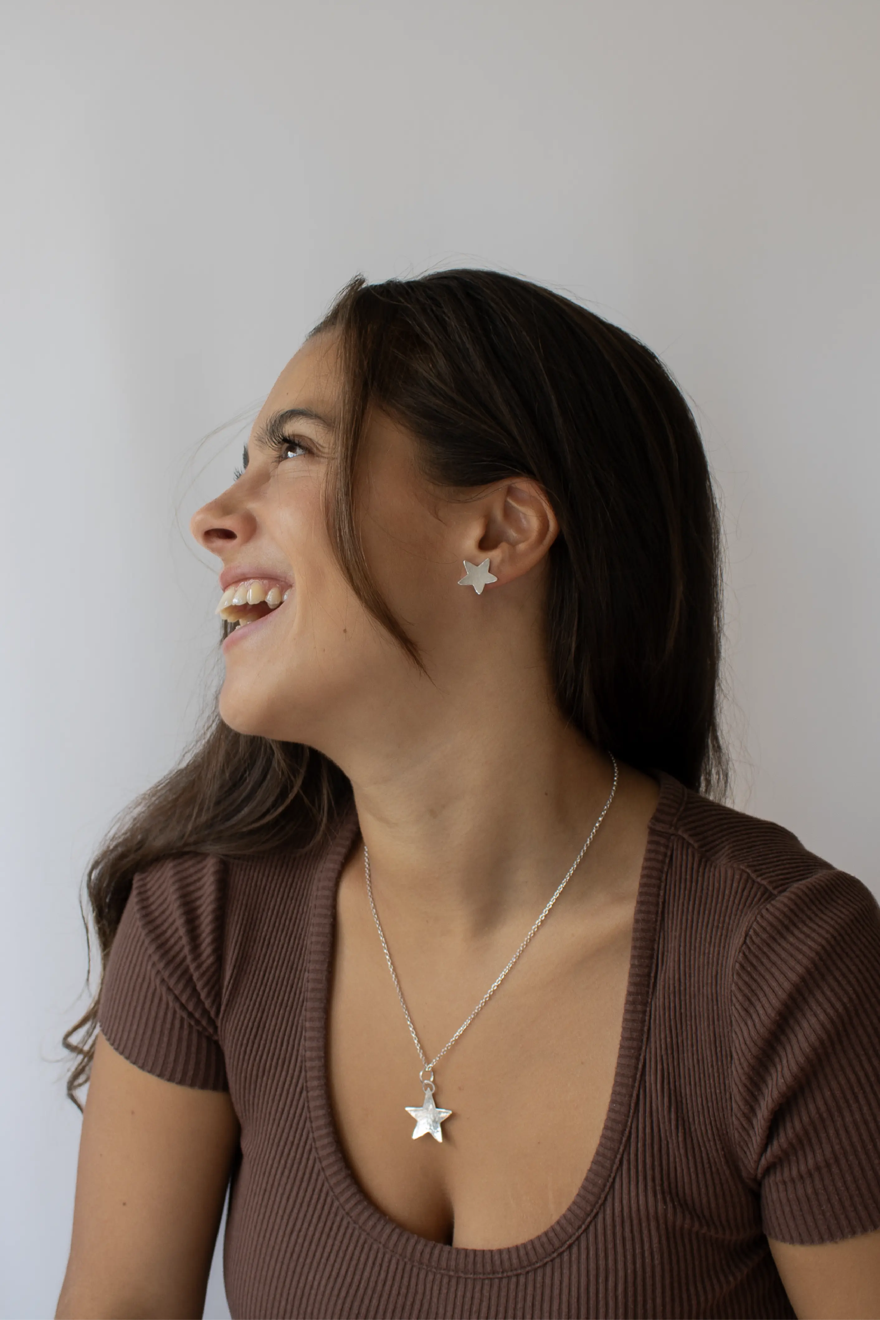 The model smiling, wearing a star shaped dimpled silver earring and a matching necklace.