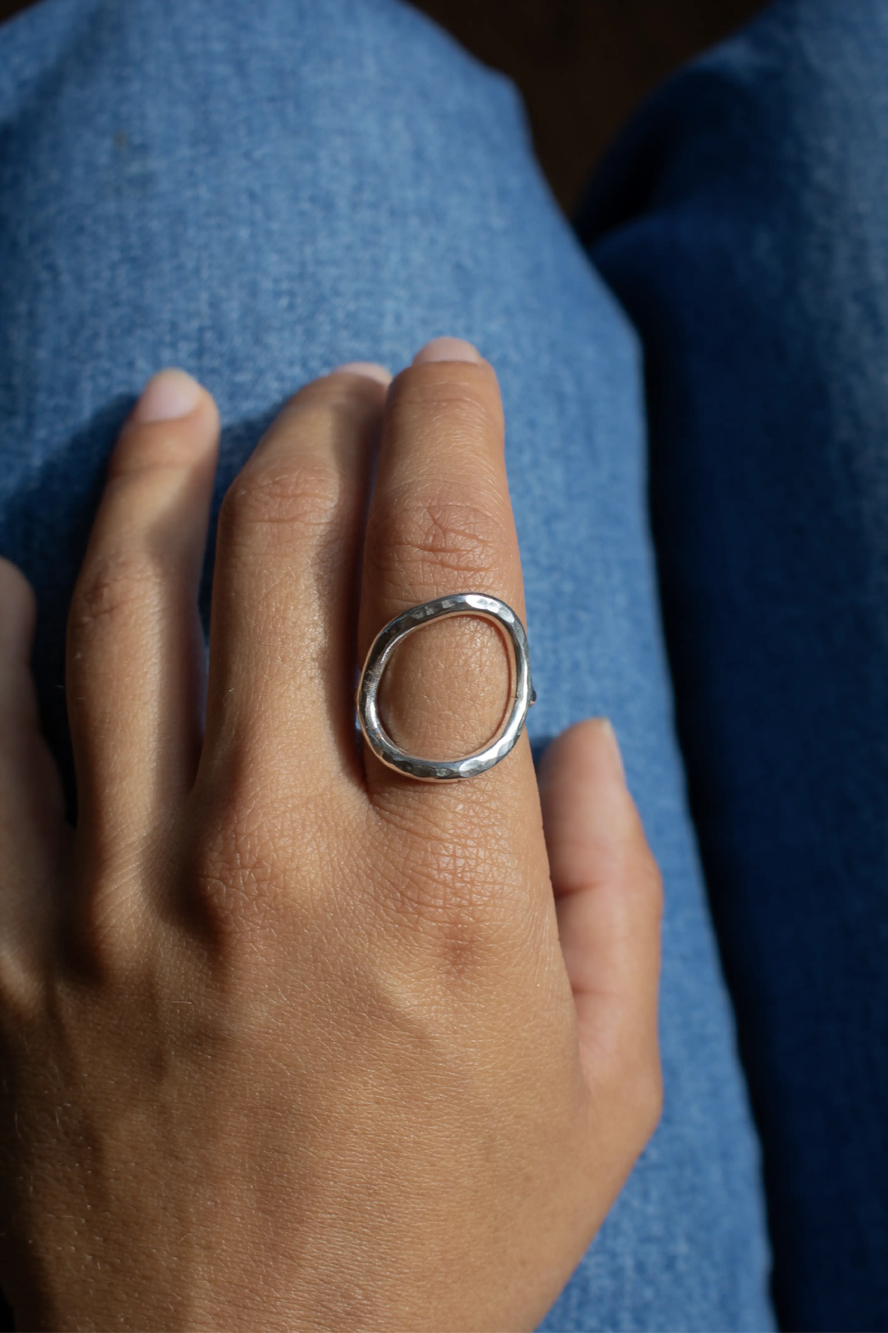 A hand waering a silver ring over a blue jeans texture background.
